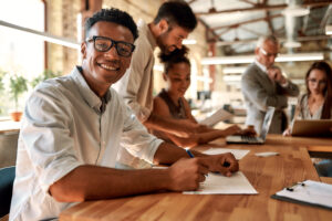 Young and cheerful afro american man in eyeglasses looking at camera with smile while working with his colleagues in the modern office